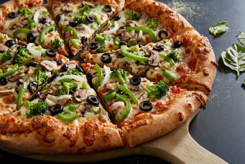 Vegetable pizza with broccoli, mushrooms, olives, onions, and green peppers on a wooden peel.