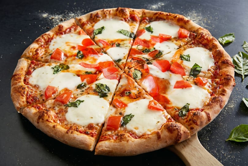 Sliced Margherita pizza with fresh mozzarella, tomatoes, and basil on a wooden peel.