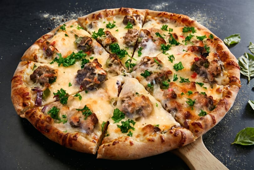 A whole sliced pizza with melted cheese, sausage, and parsley on a wooden peel.